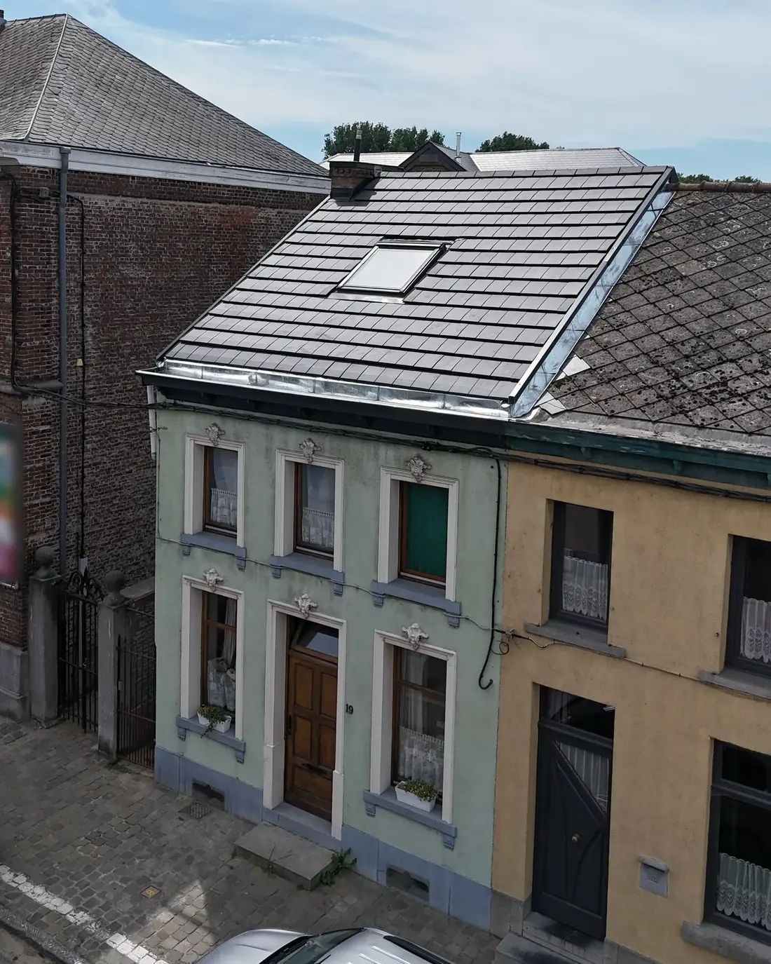 Façade d'une maison de ville vue de la rue, surmontée d'une toiture neuve en tuiles noires avec fenêtre de toit