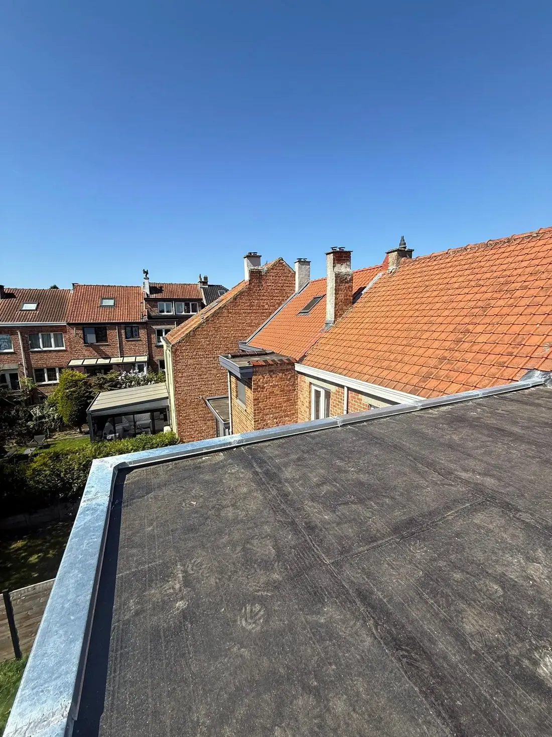 Toiture plate remise en pente et étanchéifiée avec rives en zinc, au-dessus d'une rangée de maisons en briques