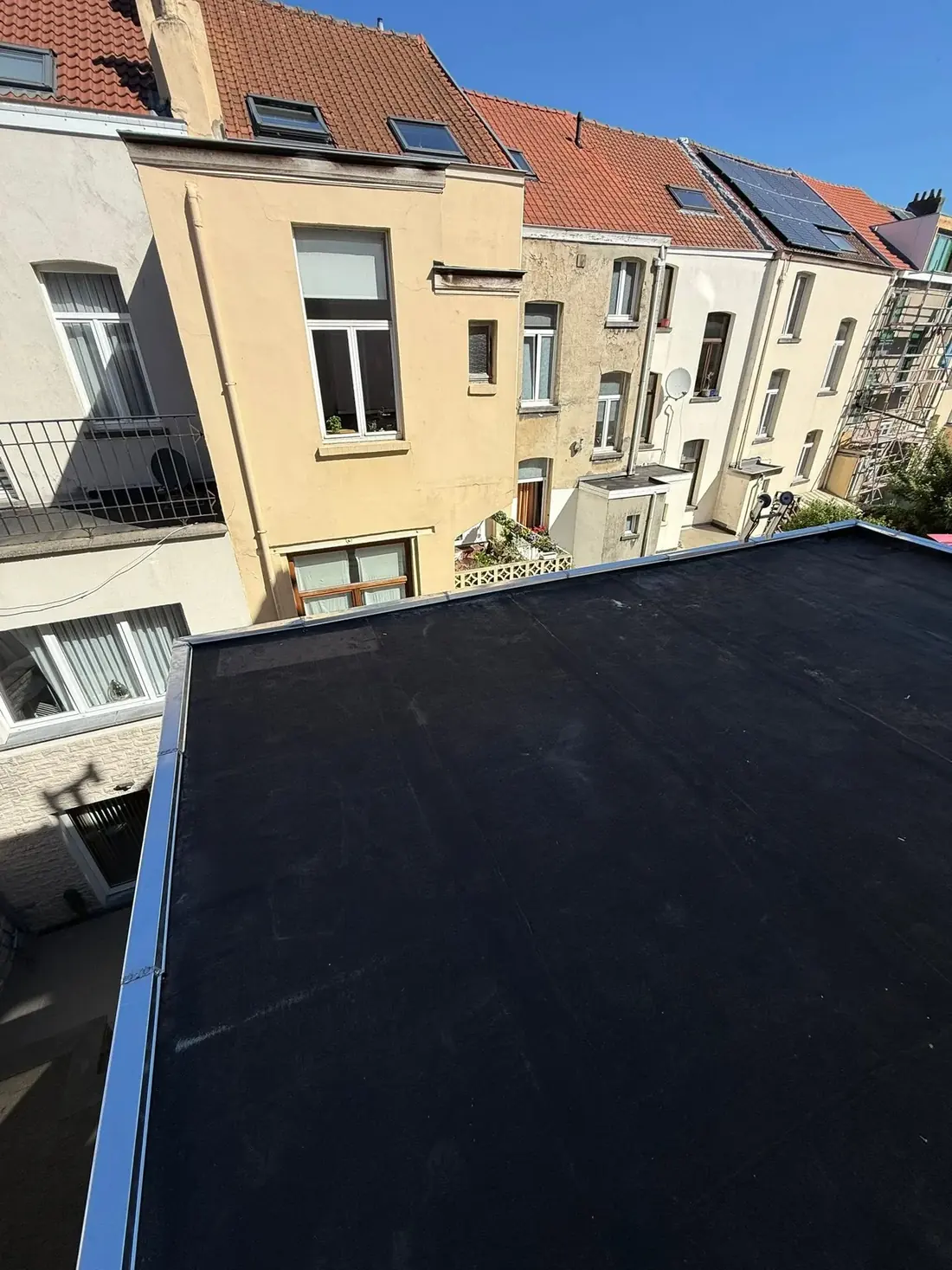 Toiture plate neuve en membrane noire dominant les jardins et les façades d'une rue de maisons de ville