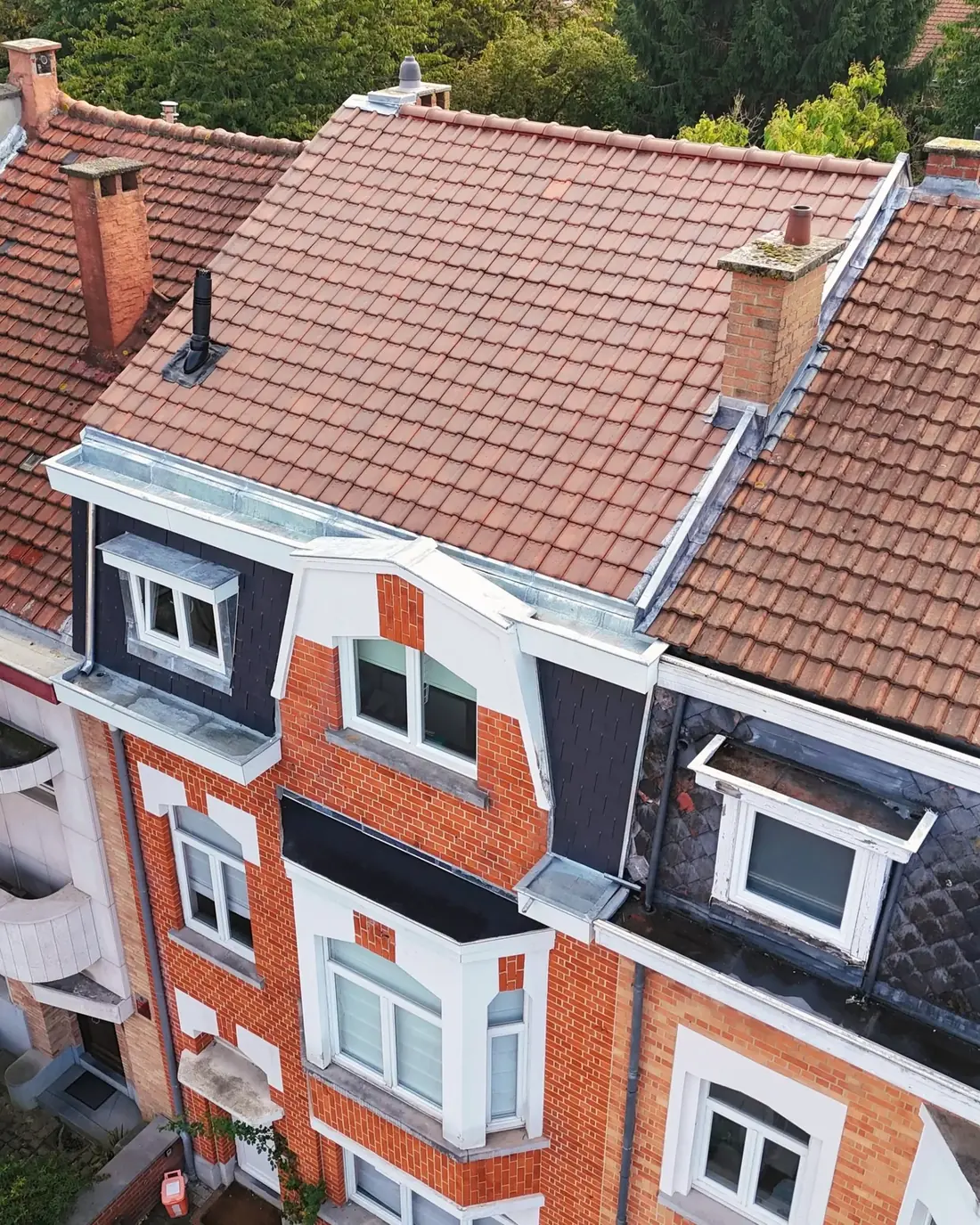 Vue de drone d'une maison de ville en briques surmontée d'une toiture neuve en tuiles rouges, avec ses solins en zinc