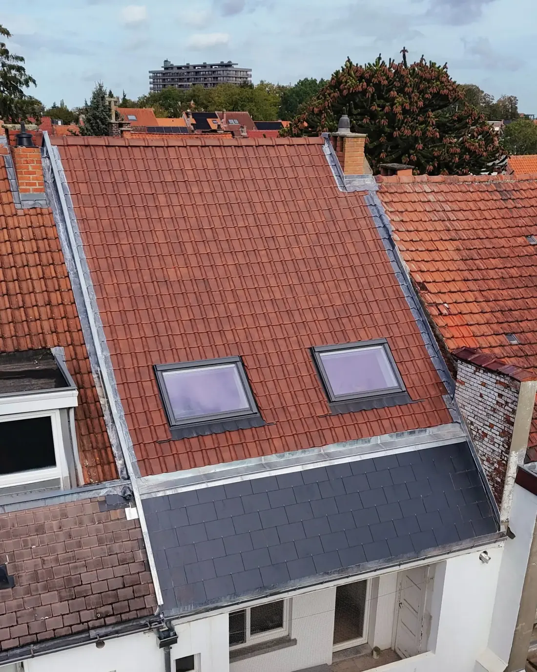 Vue de drone d'une toiture de tuiles rouges neuves avec deux fenêtres de toit, une noue en zinc et un raccord en ardoise