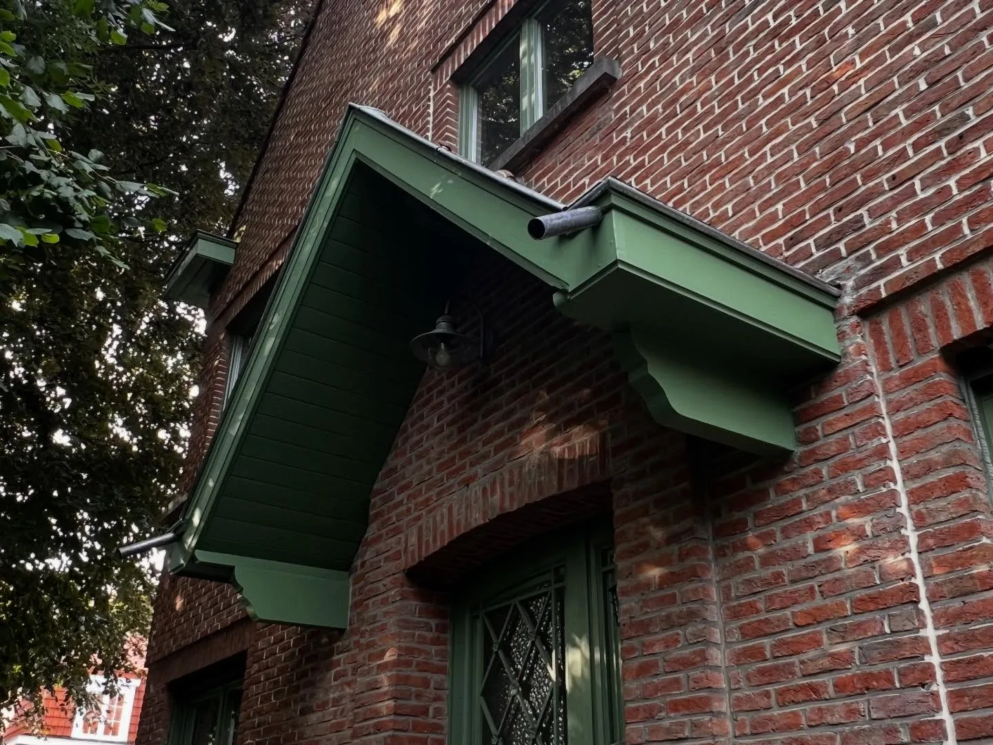 Auvent de porche remis à neuf et peint en vert, au-dessus d'une porte vitrée dans une façade en briques