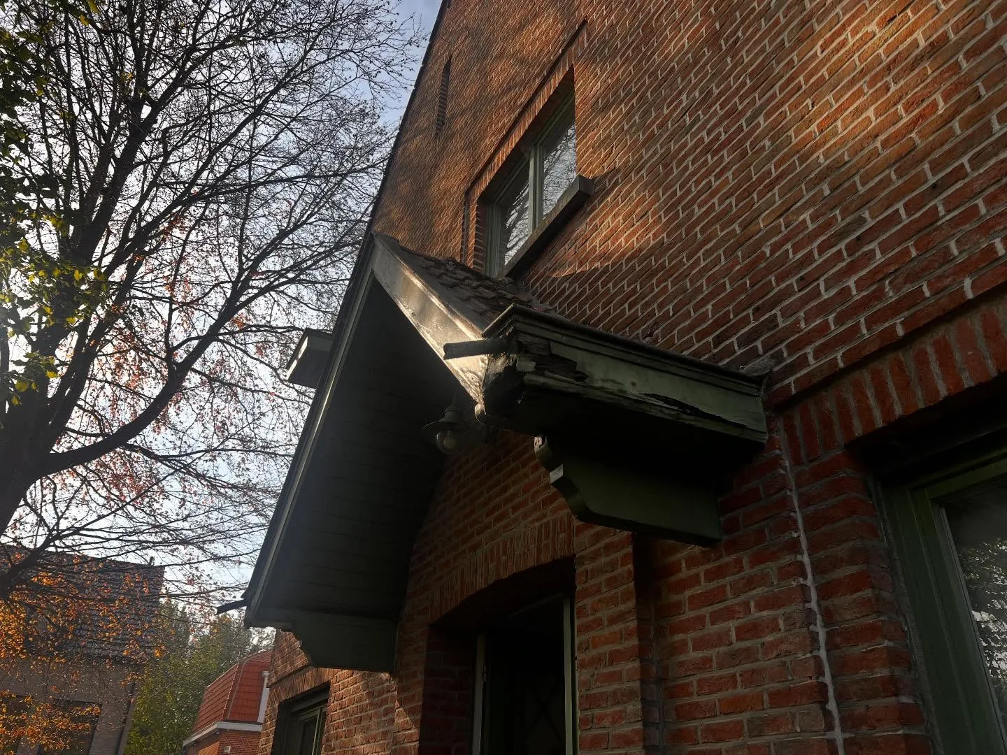 Auvent de porche ancien et sombre au-dessus d'une porte vitrée dans une façade en briques