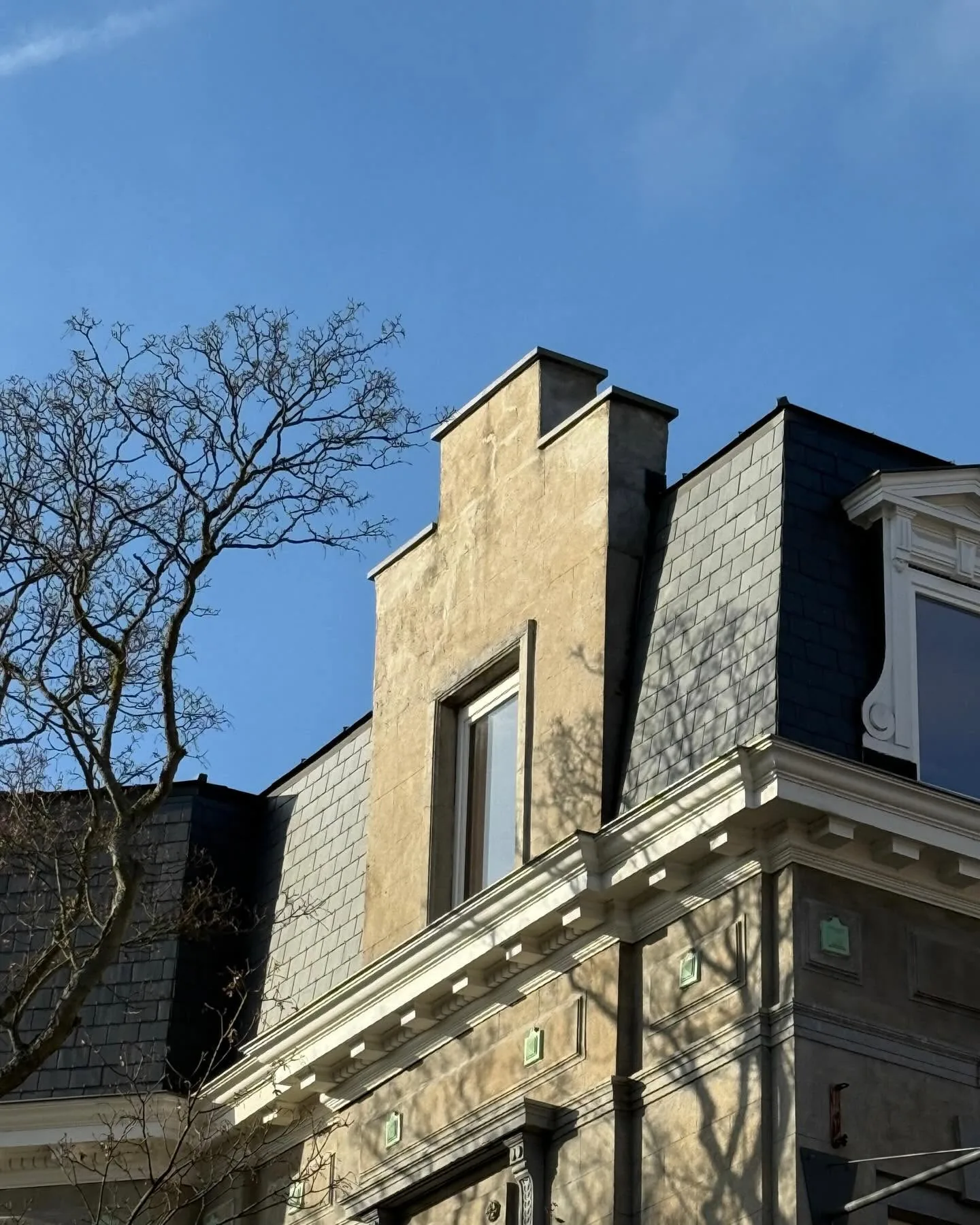 Façade de maison de maître surmontée d'une mansarde en ardoises naturelles et corniches en zinc, ciel bleu