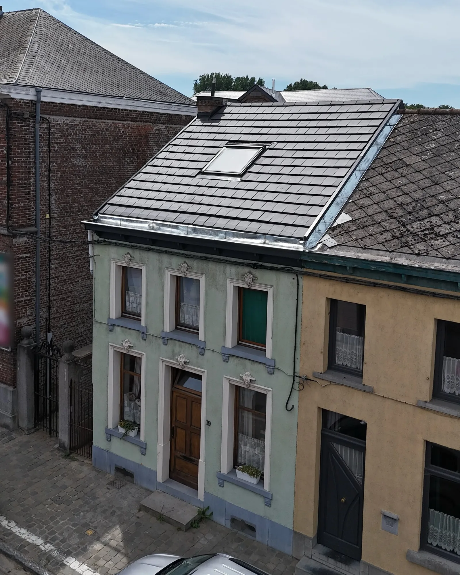 Façade d'une maison de ville vue de la rue, surmontée d'une toiture neuve en tuiles noires avec fenêtre de toit et solin en zinc