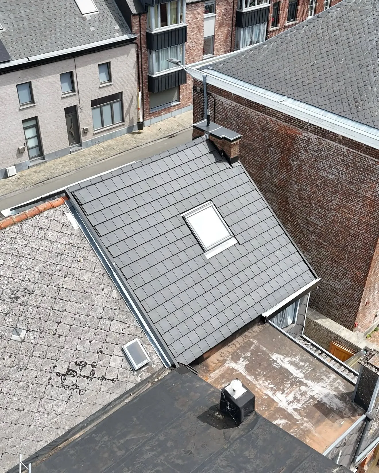 Vue de drone de la toiture neuve en tuiles noires à côté d'une toiture plate et d'une toiture voisine ancienne