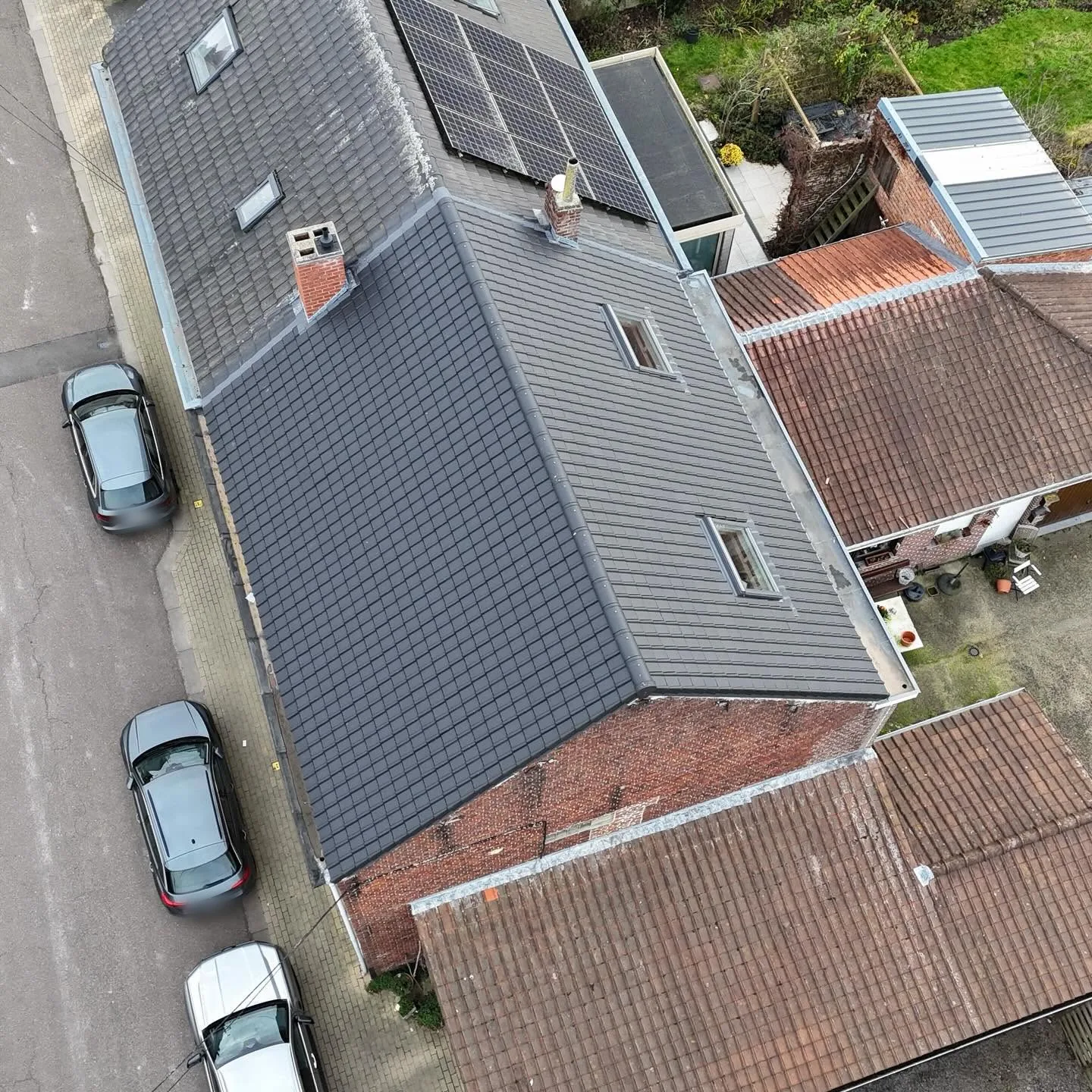Vue de drone d'une toiture de tuiles anthracite neuves avec panneaux solaires et fenêtres de toit, rue en bordure