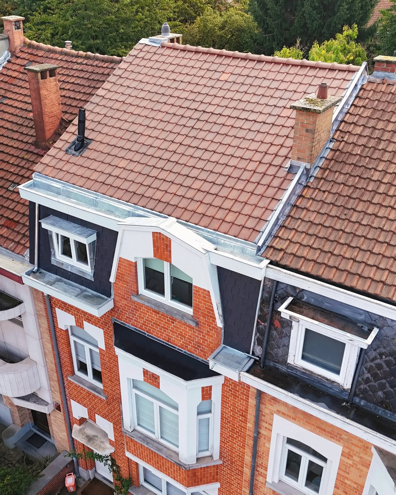 Vue de drone d'une maison de ville en briques avec sa toiture neuve en tuiles rouges, ses solins en zinc et ses fenêtres de toit
