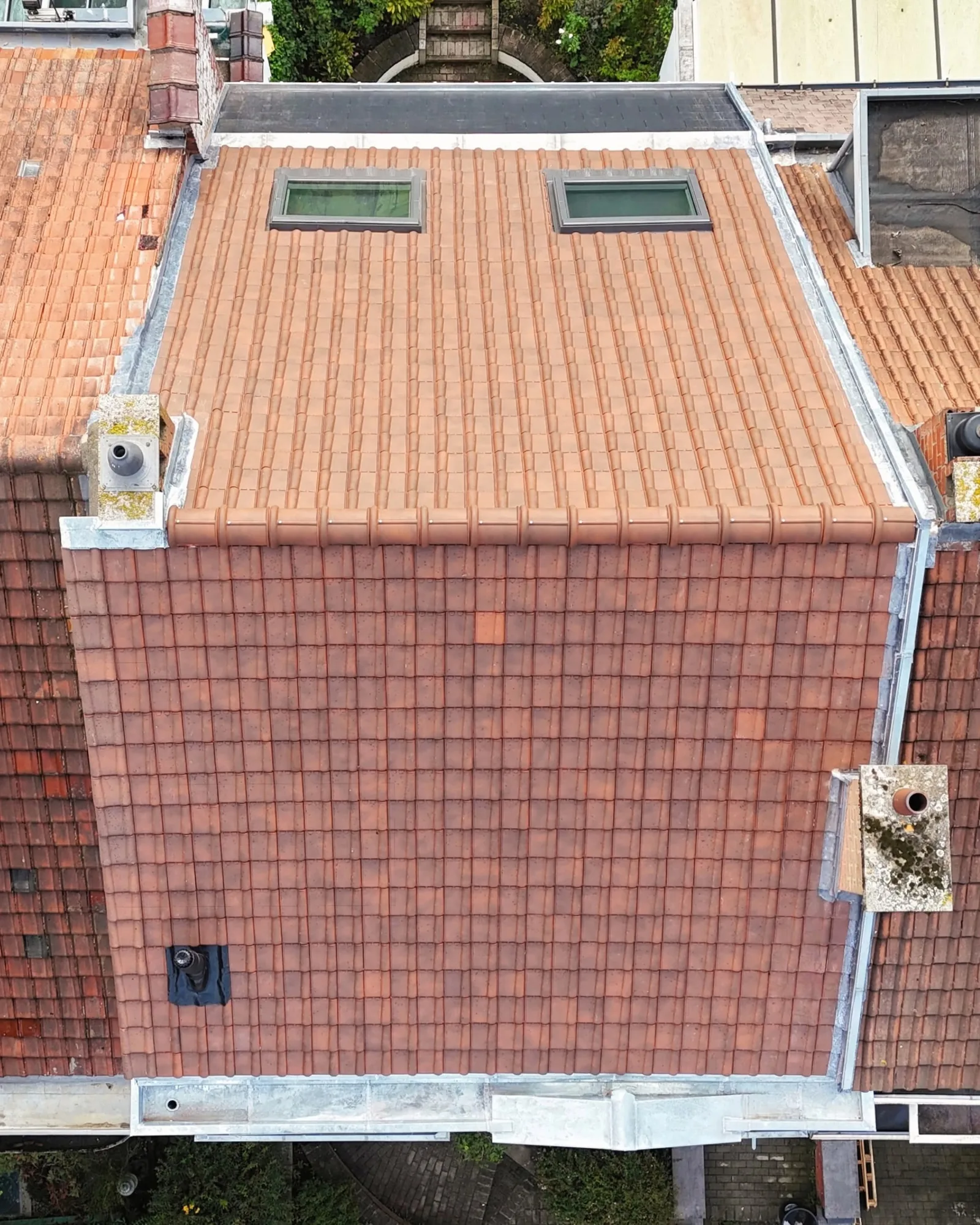 Vue de drone d'un versant de tuiles rouges neuves avec deux fenêtres de toit et des solins en zinc