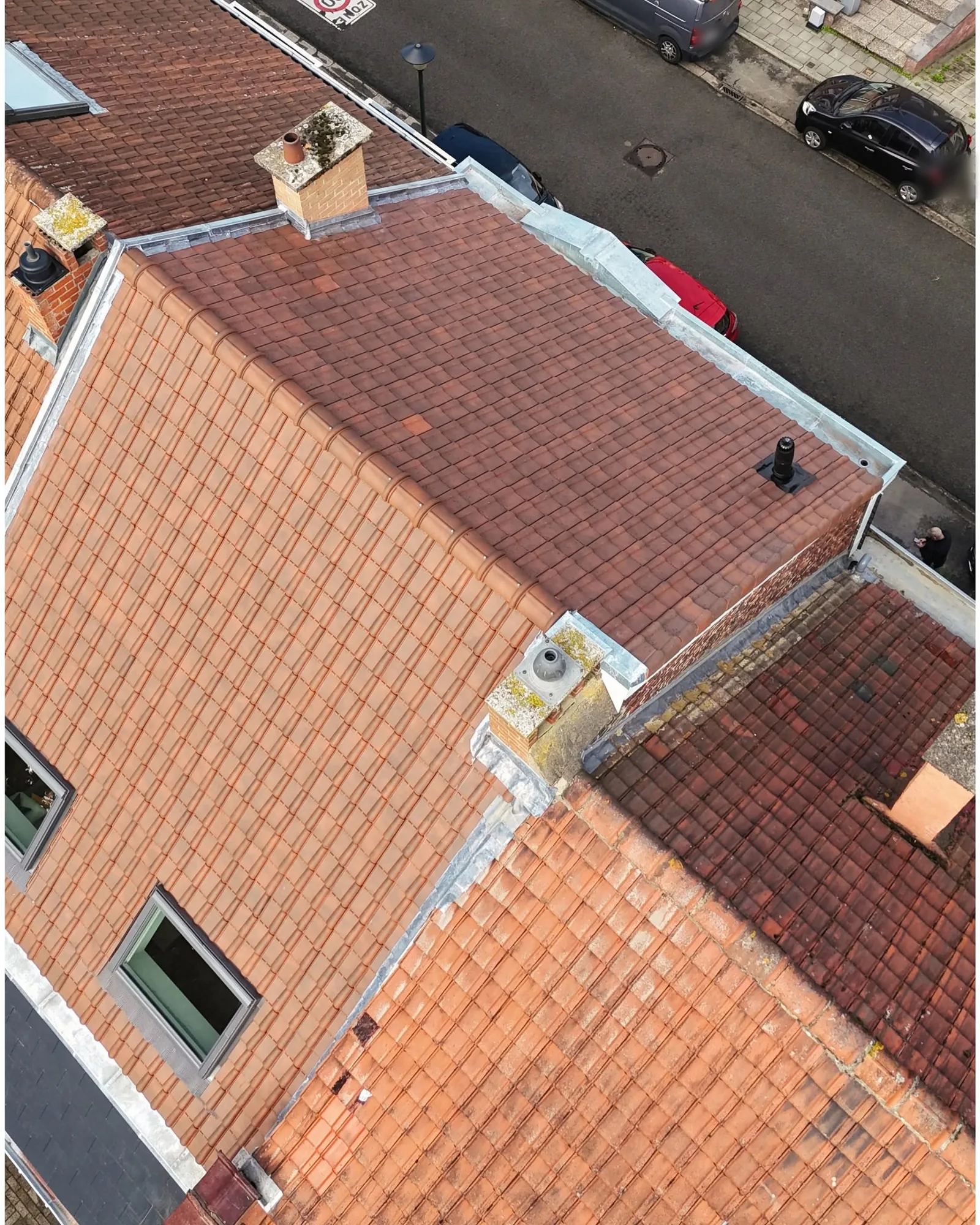 Vue de drone de toitures en tuiles rouges neuves avec souches de cheminée habillées de zinc, rue en arrière-plan