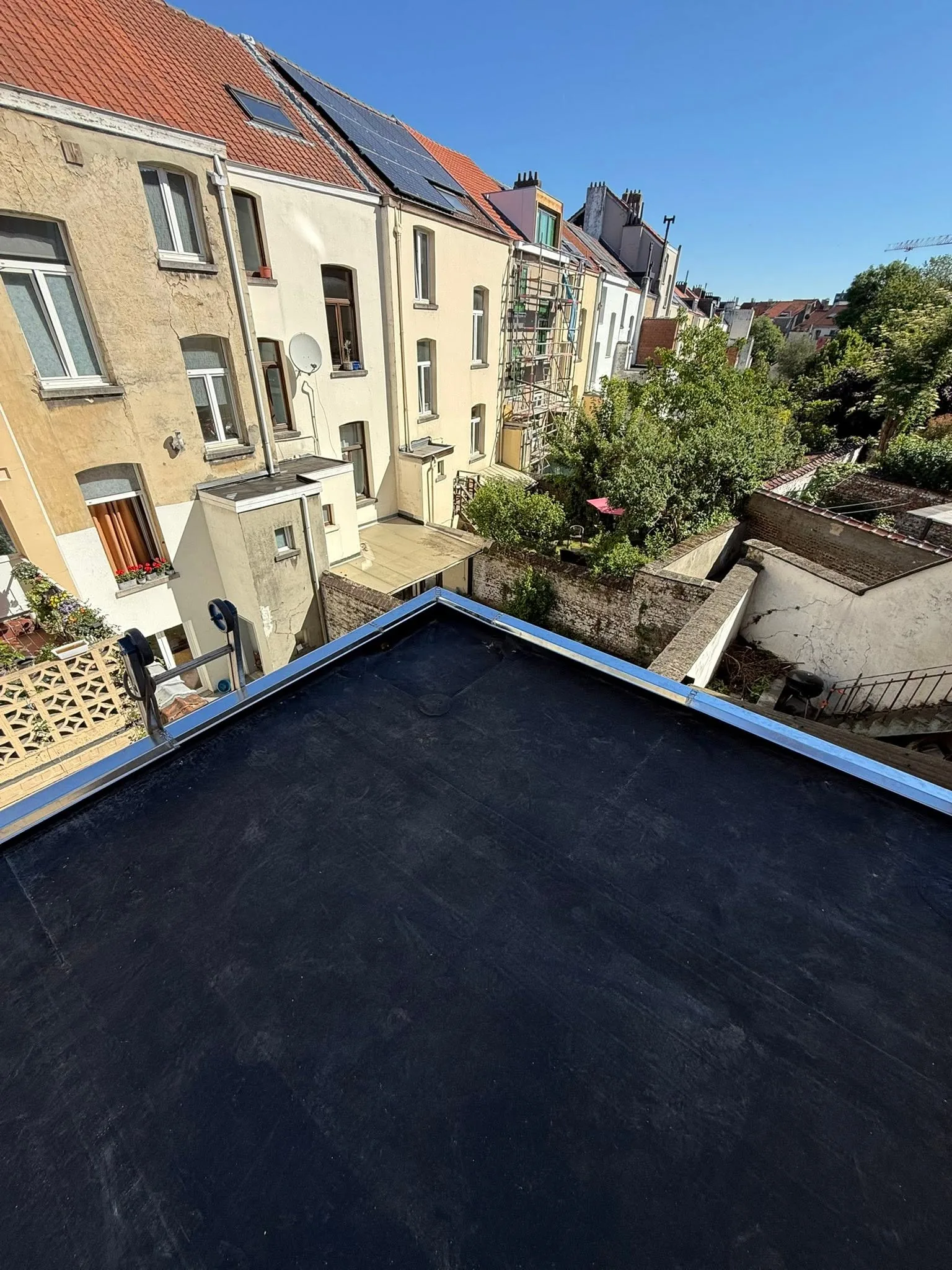 Angle d'une toiture plate neuve avec rive en zinc, derrière les maisons mitoyennes