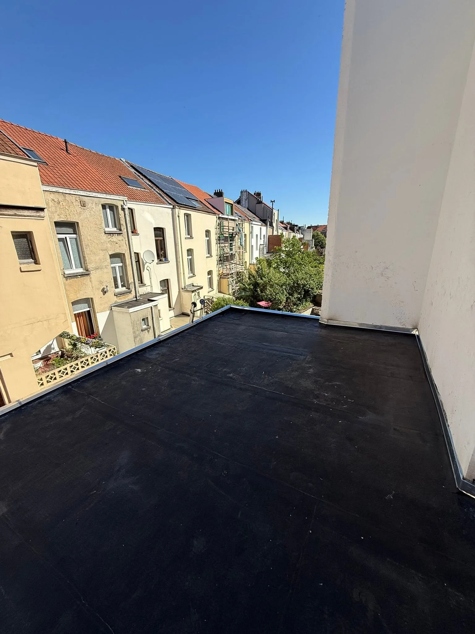 Toiture plate neuve en membrane noire contre un mur blanc, vue sur les toits de la rue