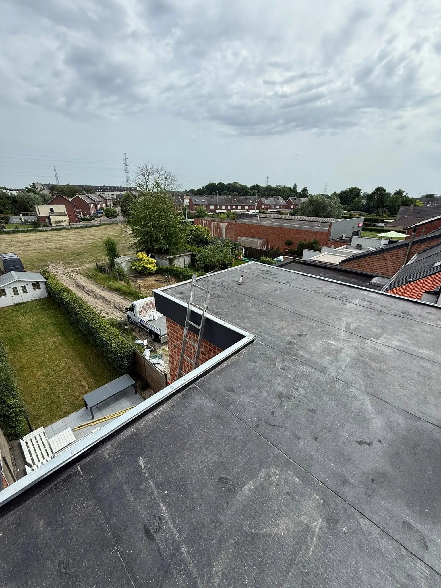 Toiture plate refaite avec sa membrane bitumineuse neuve et sa rive en zinc, campagne en arrière-plan