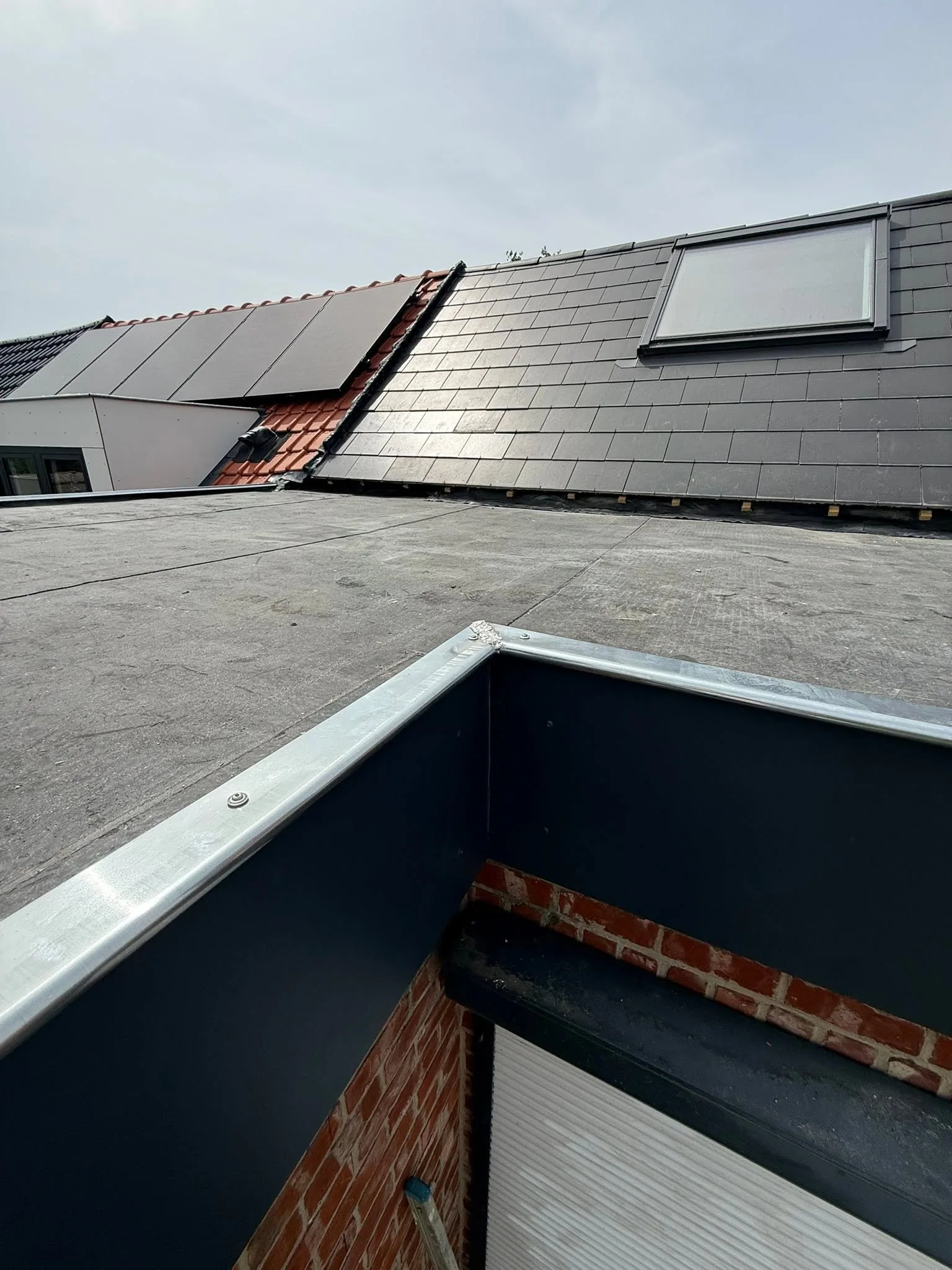 Angle de toiture plate neuve avec relevé en zinc contre une façade en briques et un versant à panneaux solaires
