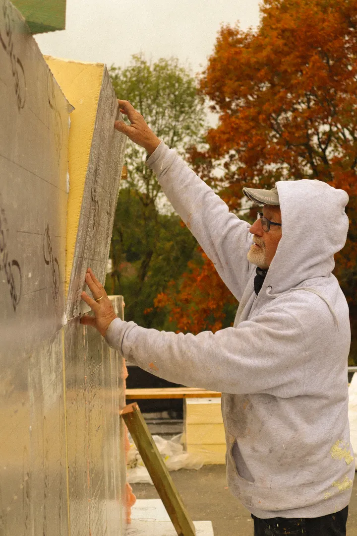 Un couvreur de l'équipe Le Fils met en place des panneaux d'isolation contre un mur, arbres d'automne en arrière-plan