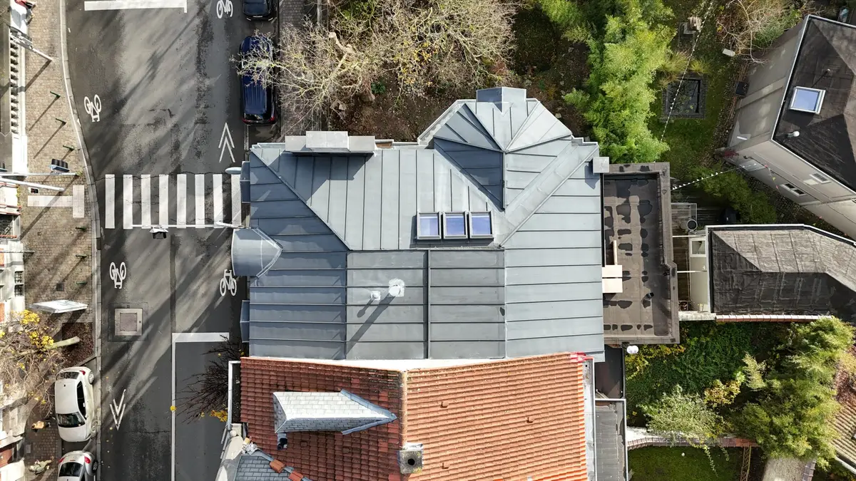 Vue de drone d'une toiture en zinc à pans multiples avec trois fenêtres de toit, en bord de rue à Bruxelles