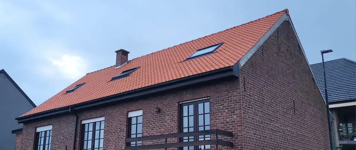Maison en briques sous un toit de tuiles rouges neuf avec fenêtres de toit et gouttière noire, ciel bleu