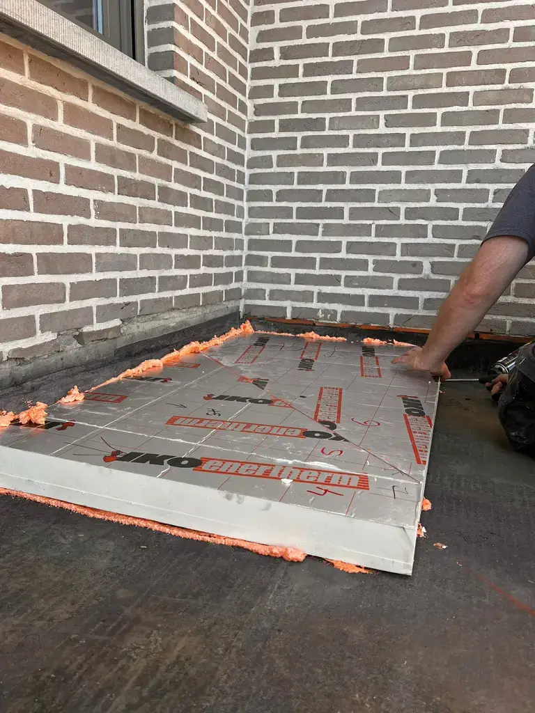 Pose d'un panneau isolant PIR sur une toiture plate en rénovation, devant un mur en briques